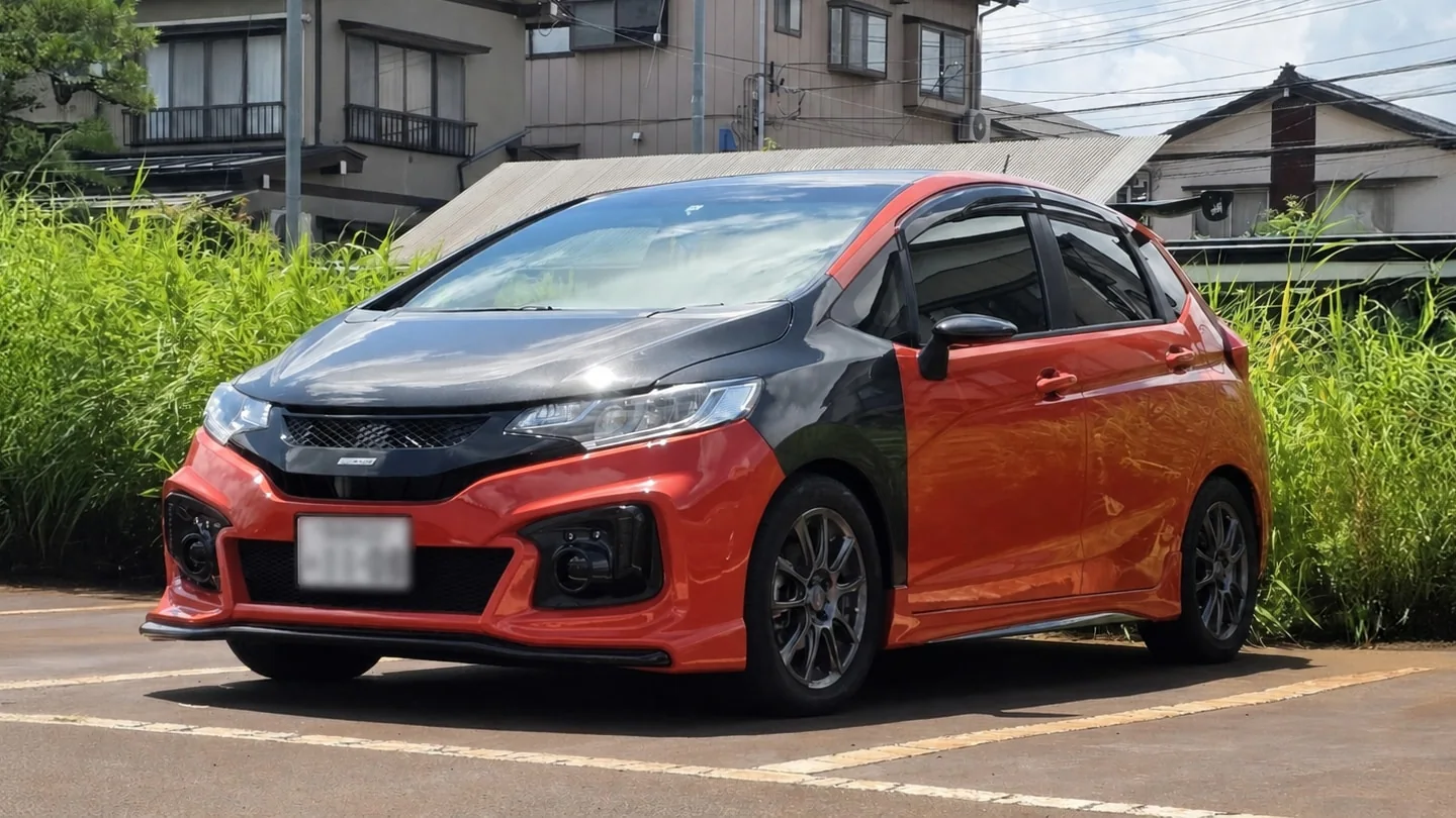 日本で停車しているオレンジのHonda Fit RS。ボンネットとフロントフェンダーはカーボン製で、ナンバープレートは読めないようぼかされている。