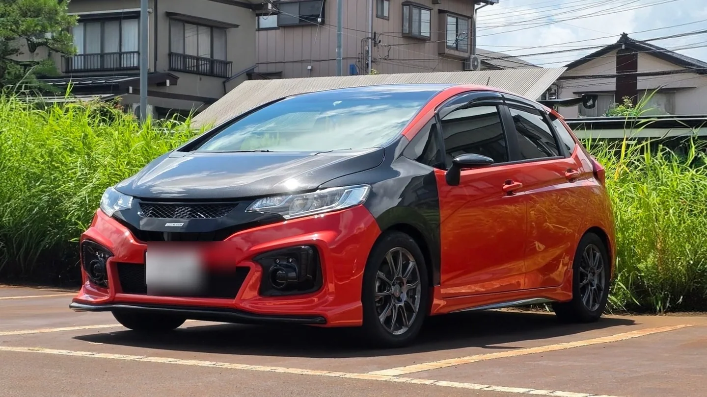 サンセットオレンジIIのHonda Fit GK5。ウェットカーボン製ボンネットとフェンダーを装着し、ナンバーはぼかされている。