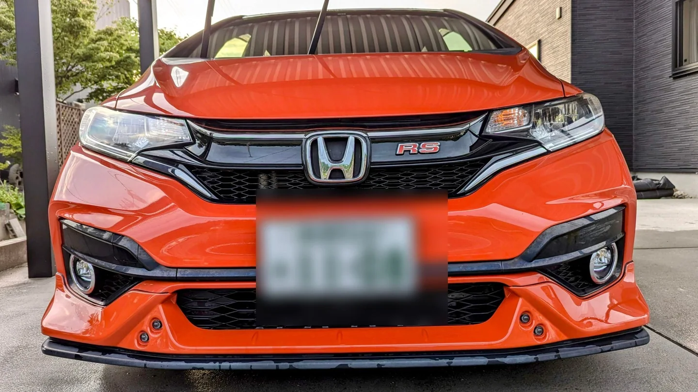 カーボン外装に交換する前のオレンジ色のHonda Fit GK5。純正ボンネットとグリルを装着し、ナンバーはぼかされている。