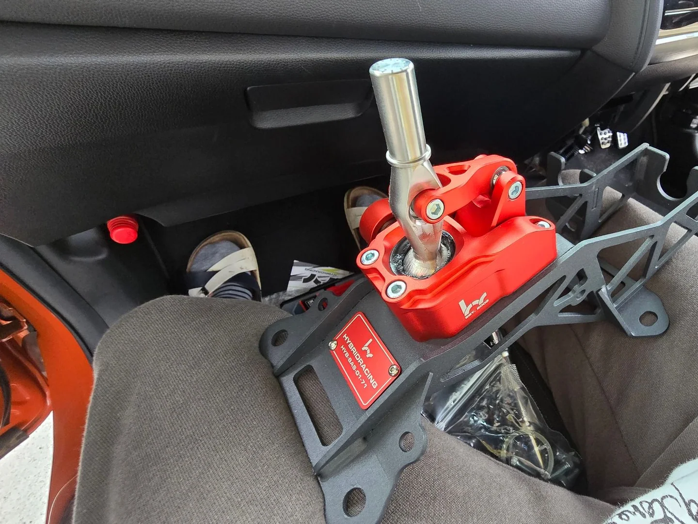 取付作業中、Honda Fitのフロントシートに置かれた赤いHybrid Racing製ショートシフター。