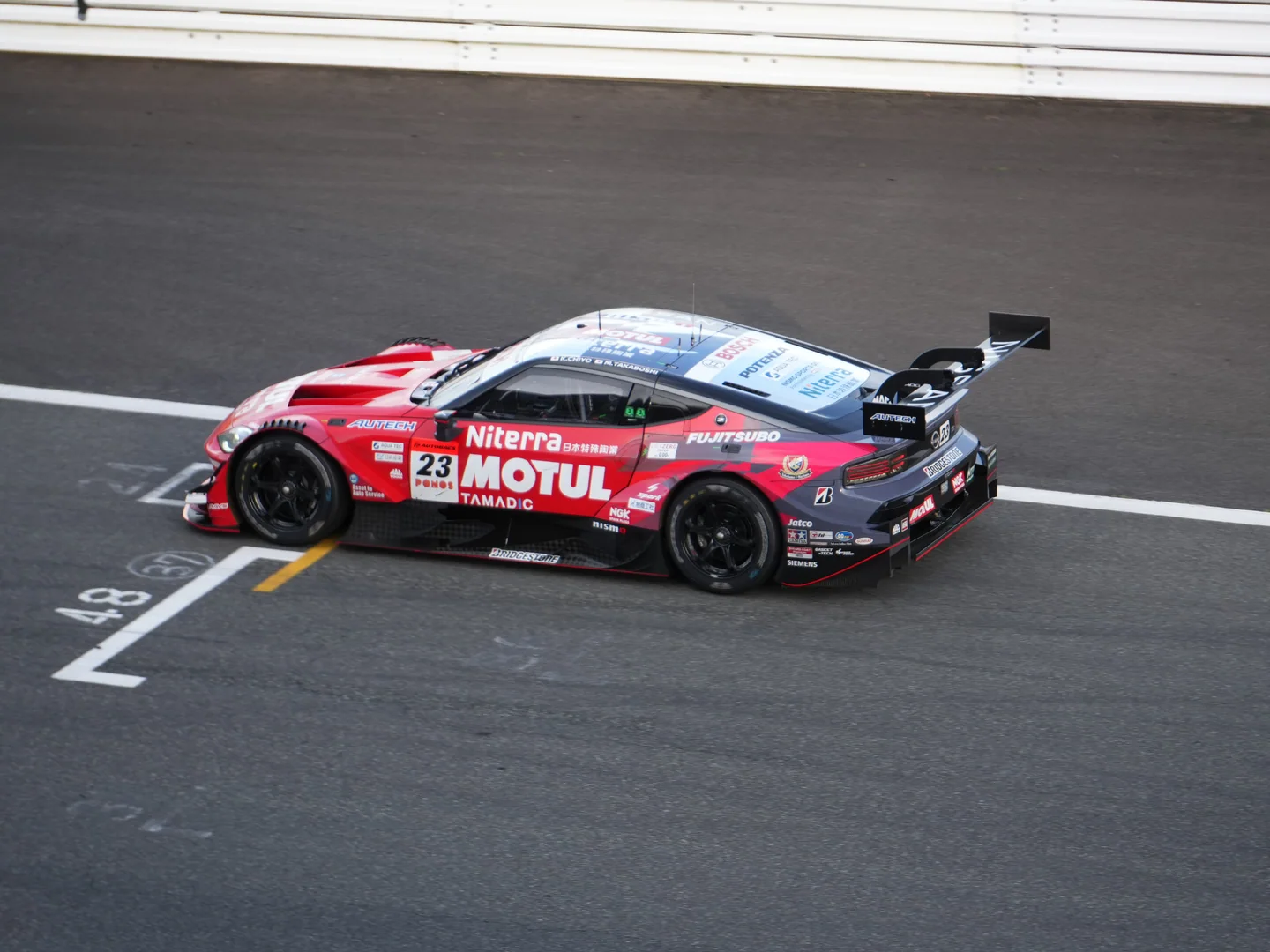 赤と黒のNo.23 MOTUL Niterra Zが富士スピードウェイのグランドスタンド下を通過する。