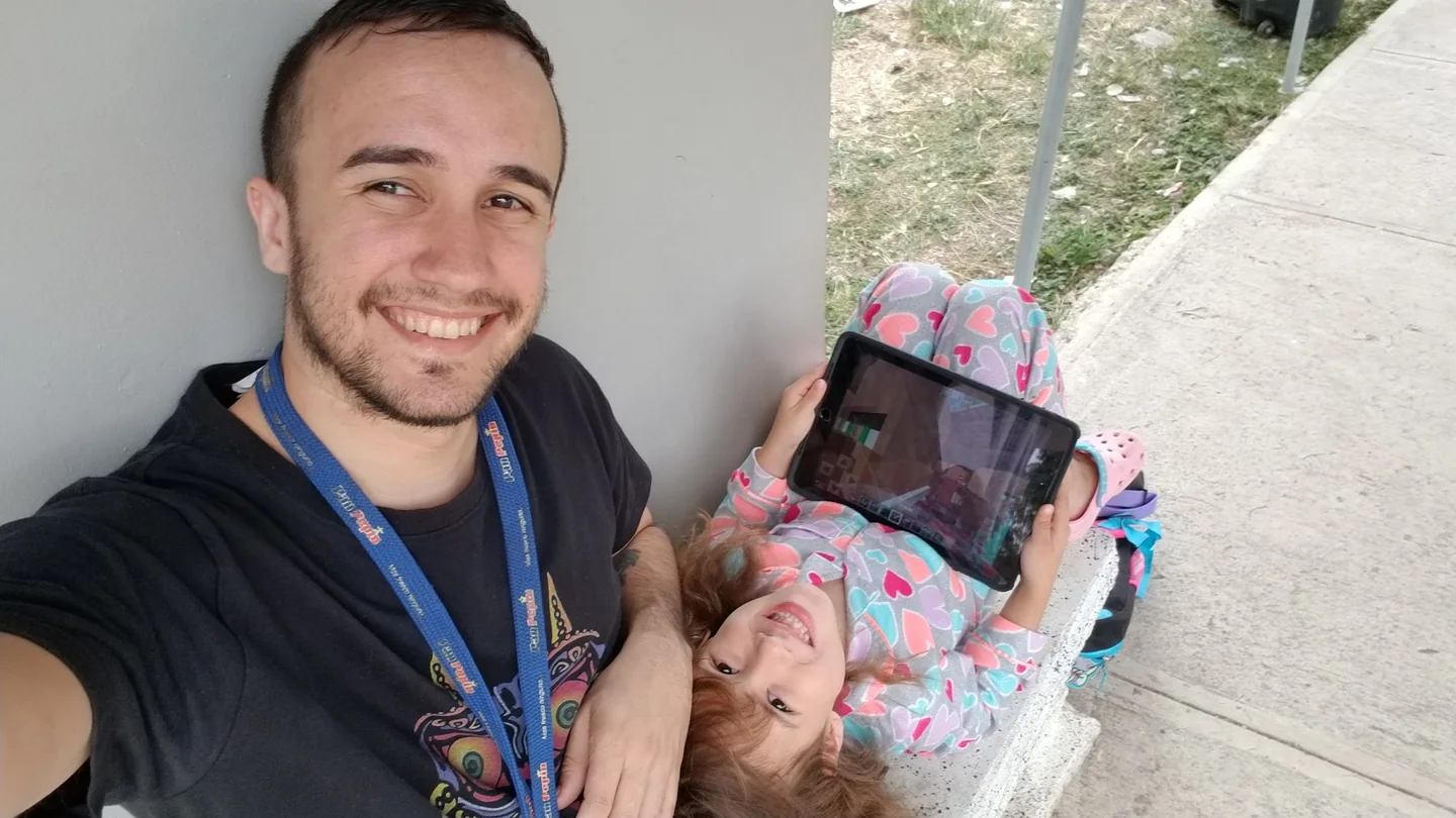 ベンチに逆さまに寝転がってタブレットでMinecraftを遊ぶ娘と、その隣で笑うハリー。