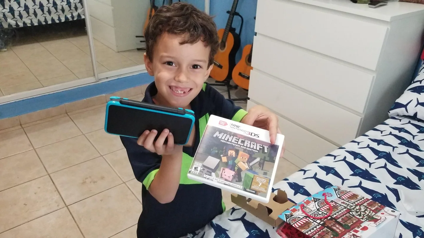 携帯ゲーム機とゲームソフトを手にして笑う七歳の男の子。