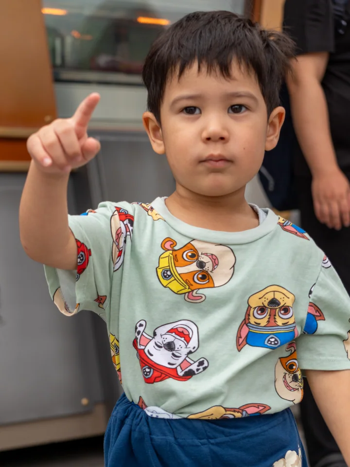 The youngest son points decisively ahead while wearing a shirt covered in cartoon rescue dogs.
